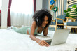 © kanpisut - Woman lying on floor and using laptop at home in living room