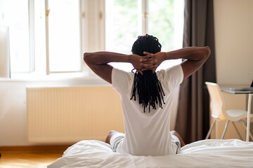 Morning Routine. Young Black Man Sitting On Bed With Hands Behind Head