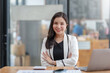 © amnaj - Asian business woman sitting with her arms crossed and confidently looking at the camera and focused on her work in the office.