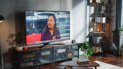 Wall Mural - Living Room Television Showing TV News Programme with Two Presenters Talking and Joking on TV. Live Broadcast of The Popular Talk Show. Cozy Apartment Living Room with Stylish Loft Interior Concept.