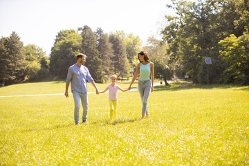 Wall Mural - Happy young family with cute little daughter having fun in the park on a sunny day