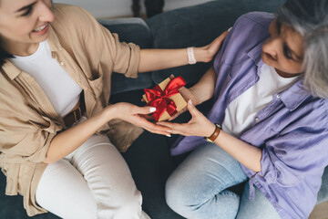 Cheerful women giving present to senior mother for birthday