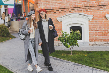 Young female best friends talking to each other discussing interesting themes during free time hipster girls joking and having fun together enjoying recreation with coffee to go on urban background