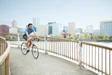 Young Male Athlete Riding Bicycle On Bridge By River In City