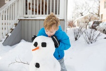 Boy Eating Snow While Making Snowman In Yard