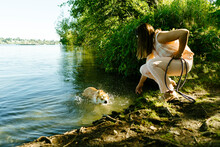 Side View Of A Woman Crouching Next To A Swimming Dog