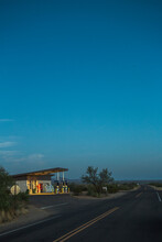 A Vintage Gas Station Glows Beside An Empty Desert Road At Dawn