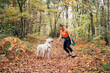 © Daniel Gonzalez/Stocksy - Happy woman with her dog in a forest with brown leaves on the ground
