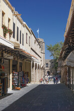 Rhodes, Greece: Tourists Wander Down A Narrow Street Of Shops In The Medieval 14th-century Fortified City On An Island In The Cyclades Of Greece.