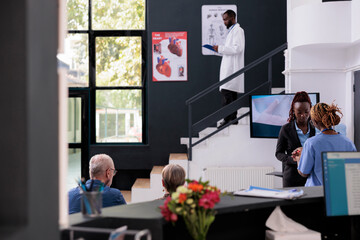 Wall Mural - Medical assistant talking with receptionist discussing patients appointment while working in hospital waiting area. People having checkup visit consultation with doctor, planning health care treatment