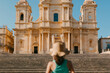© Jimena Roquero/Stocksy - Tourist with hat in front of Palazo Nicolaci in Noto, Sicily.