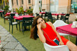 © Jimena Roquero/Stocksy - brunette woman smiling at camera sitting on restaurant terrace