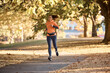 © Drazen - Full length of female athlete jogging in autumn park.