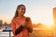 © Drazen - Happy athletic woman texting on cell phone outdoors at sunset.