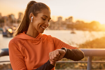 Wall Mural - Happy sportswoman using fitness tracker while exercising at sunset.