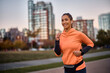 © Drazen - Happy athletic woman listens music on earphones while jogging in park.