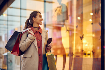 Happy woman with shopping bags looking at store windows while walking through city.