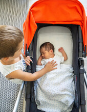 Boy Caressing His Newborn Sister While She Sleeps In Her Stroller