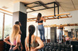 © Pedro Merino/Stocksy - Woman doing pull-ups in the gym with her training partners