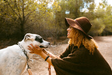 Girl With Hat And Poncho Patting Her Dog Smiling Outdoor In Sunlight