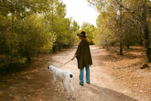 Back Of Girl With Hat And Poncho Walking Her Dog In Forest 