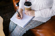 © Serena Burroughs/Stocksy - Woman holding beverage and writing down a to do list at a cafe
