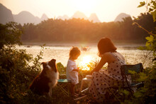 Asian Mother And Daughter Having Picnic By The River At Sunset Time