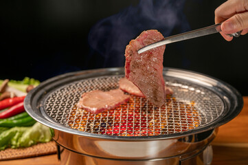 Canvas Print - Hand using chopsticks to pick up Wagyu Beef on hot charcoal Asian BBQ food style, Grilled Beef Sirloin meat on the charcoal stove,Korean BBQ style.