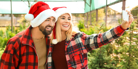 Sticker - Couple taking selfie while choosing Christmas tree in greenhouse