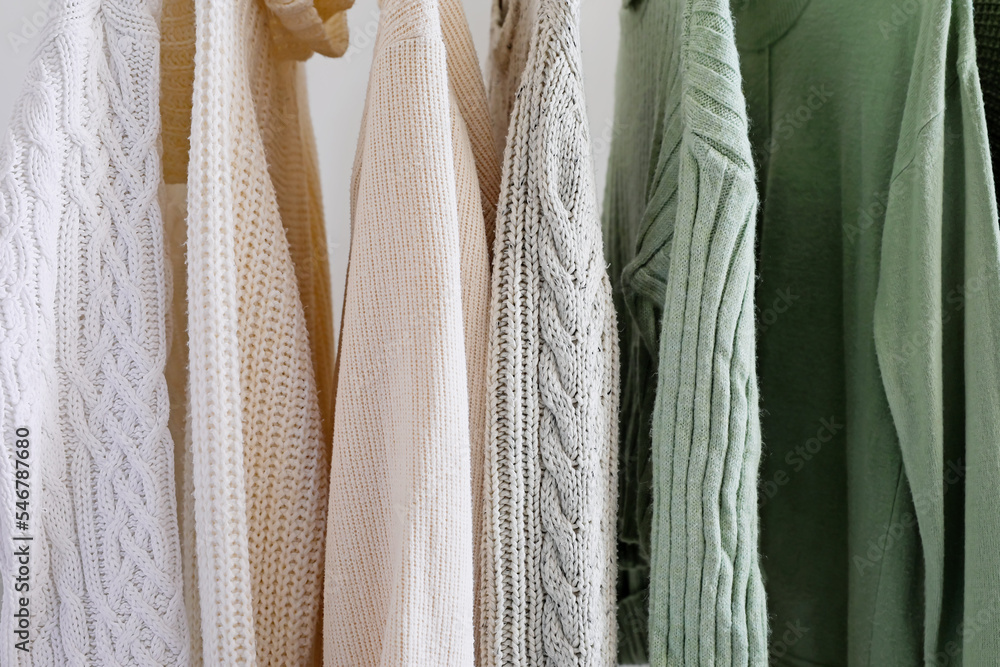 Rack with knitted sweaters near light wall, closeup