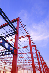 Wall Mural - Low angle view of red and black metal castellated beam of large industrial building structure in construction site against sunset sky background in vertical frame