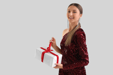 Poster - Young woman in red dress with Christmas gift on grey background