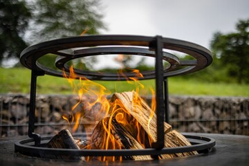 Canvas Print - Metal fire pit with the wood burning in the hot flames on a natural blurred background outside