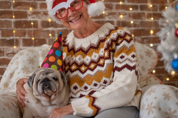 Wall Mural - Funny holiday christmas time with alternative couple senior woman and funny dog pug together on the sofa near the christmas tree - winter home lifestyle with animals at home