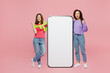 © ViDi Studio - Full body young two friends fun women wear green purple shirts near big huge blank screen mobile cell phone smartphone with area do winner gesture isolated on pastel plain light pink color background