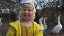 Close-uo Of A Cute Little Girl Standing On The Background Of A Herd Of The Goose