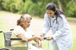 © GAJENDRRA BHATI  - alzheimer. Indian doctor check pulse with oximeter device on finger of senior female diabetes patient in a wheelchair outdoor at park. Health care, Aging. Caregiver