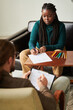 © AnnaStills - African American patient having art therapy at consultation with psychologist, she sitting at table and drawing with pencils