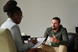 © AnnaStills - Young man having consultation with psychotherapist, he talking to her while she making notes