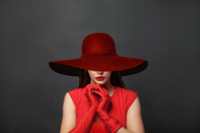 Stylish Woman Brunette With Makeup And Dark Hair Wearing Red Dress And Red Silk Gloves And Red Wide Broad Brim Hat On Black Background