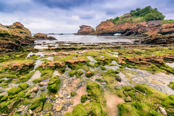 Wall Mural - Scenic view of shoreline with rocks and shallow water at Biarritz, France against dramatic storm sky