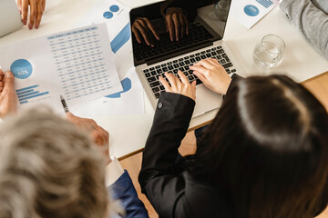 Wall Mural - Top view of a businesswoman working on a laptop in the office. Multiracial group of entrepreneurs gathered to share positive business statistics