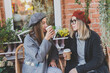 Young female best friends talking to each other discussing interesting themes during free time hipster girls joking and having fun together enjoying recreation with coffee to go on urban background