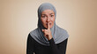 © Andrii Iemelianenko - Shh be quiet please. Portrait of millennial muslim woman in hijab presses index finger to lips makes silence gesture sign do not tells secret. Young arabian girl posing on beige studio background