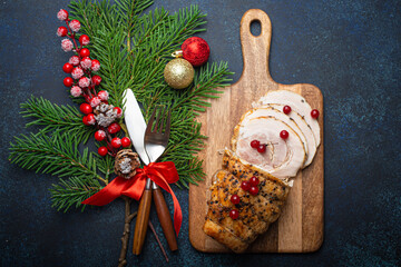 Wall Mural - Christmas baked ham sliced with red berries and festive decorations on wooden cutting board, dark rustic background from above. Christmas and New Year holiday dinner with baked pork 