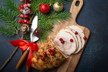 Wall Mural - Christmas baked ham sliced with red berries and festive decorations on wooden cutting board, dark rustic background from above. Christmas and New Year holiday dinner with baked pork 