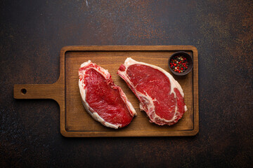 Canvas Print - Two raw uncooked meat beef rib eye marbled steaks on wooden cutting board with seasonings on dark rustic background ready to be grilled from above, preparing dinner with meat