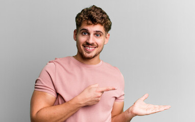 Wall Mural - young adult caucasian man smiling, feeling happy, carefree and satisfied, pointing to concept or idea on copy space on the side