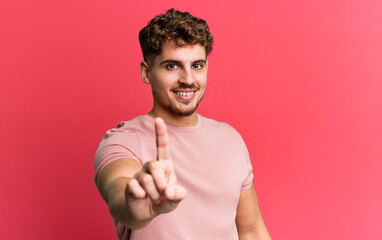 Wall Mural - young adult caucasian man smiling proudly and confidently making number one pose triumphantly, feeling like a leader