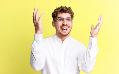 Wall Mural - young adult caucasian man feeling happy, amazed, lucky and surprised, celebrating victory with both hands up in the air